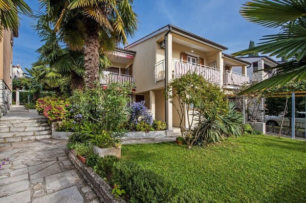 A two-story building with a balcony, surrounded by lush greenery and a well-maintained lawn.