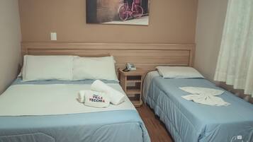 Habitación de hotel con dos camas, cada una con cubrecama azul y almohadas blancas. En la pared, un cuadro con una bicicleta rosa, una mesita de noche con un teléfono y una toalla con texto.
