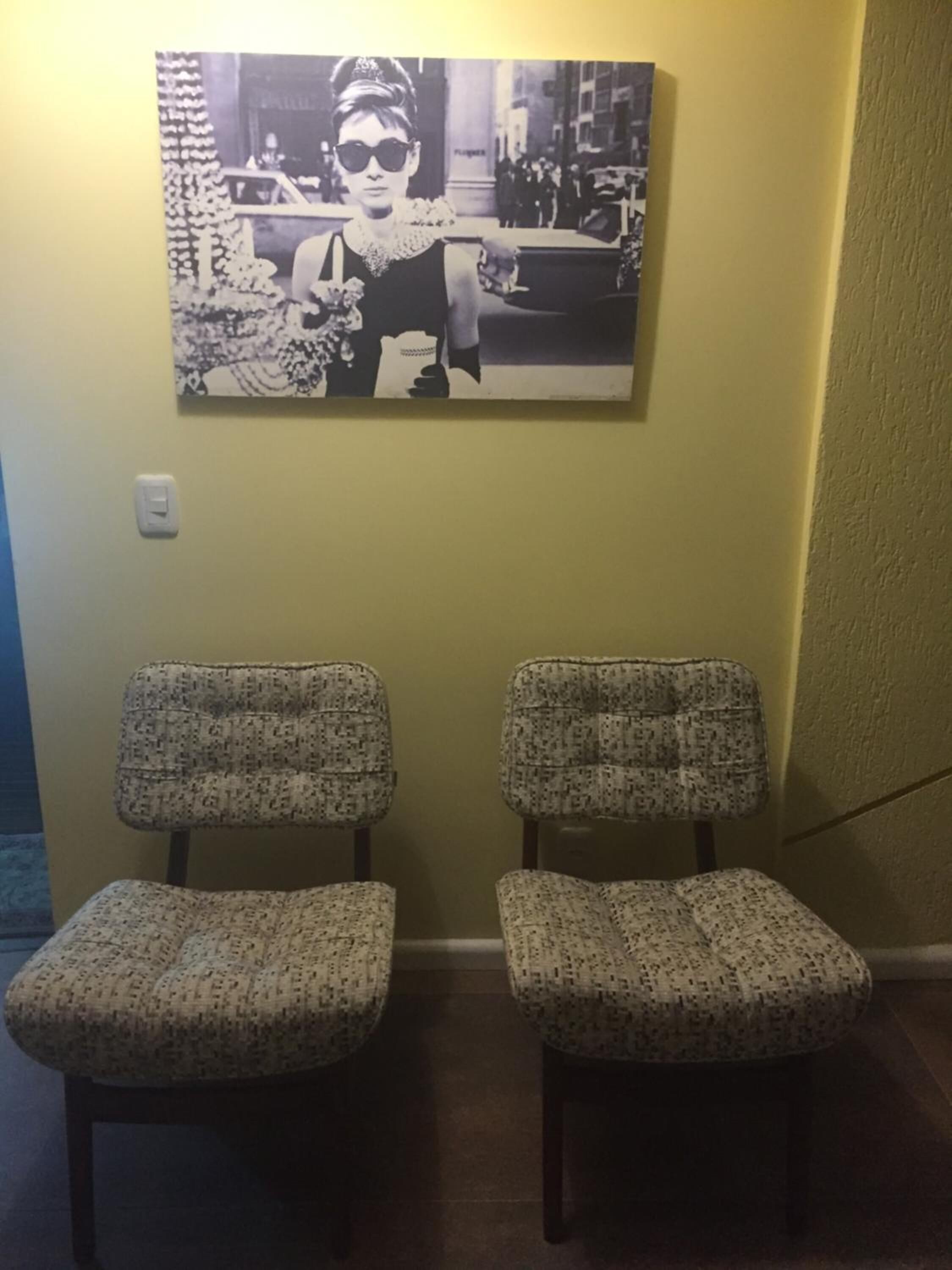 Two patterned chairs against a yellow wall, with a black and white photo above them.