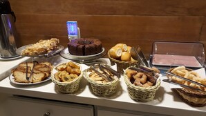 A buffet table with various baked goods, including bread, pastries, and a cake, along with a coffee machine and a microwave. - Pousada Villa Vecchia (Canela)