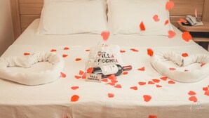 A neatly made bed with a white pillow, a bottle of wine, and a bag with text on it. - Pousada Villa Vecchia (Canela)
