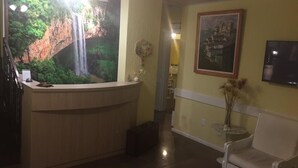 A reception area with a reception desk, a white sofa, a painting on the wall, and a television. - Pousada Villa Vecchia (Canela)