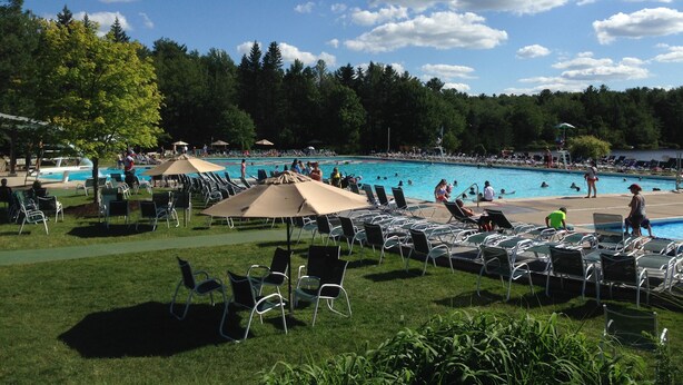 A pool area with multiple swimming pools, lounge chairs, and umbrellas. - New, Modern Streamfront 3 Bedroom. Walking Distance To Pool And Lake (Pocono Pines)