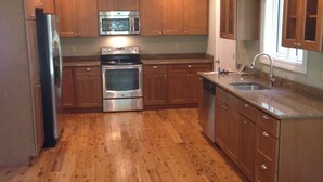 A kitchen with wooden cabinets, stainless steel appliances, and a wooden floor. - New, Modern Streamfront 3 Bedroom. Walking Distance To Pool And Lake (Pocono Pines)
