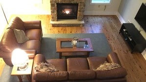 A living room with a stone fireplace, leather sofas, a coffee table, and a TV stand. - New, Modern Streamfront 3 Bedroom. Walking Distance To Pool And Lake (Pocono Pines)