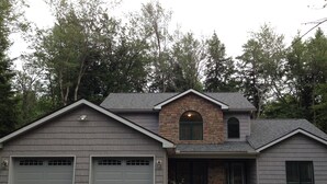 A two-story house with a stone archway entrance, two attached garages, and a landscaped front yard. - New, Modern Streamfront 3 Bedroom. Walking Distance To Pool And Lake (Pocono Pines)