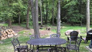 A round metal table with six chairs, surrounded by trees in a wooded area. - New, Modern Streamfront 3 Bedroom. Walking Distance To Pool And Lake (Pocono Pines)