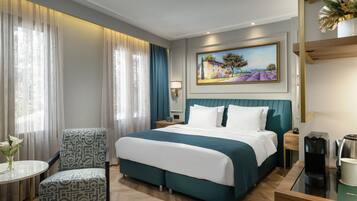 Una habitación de hotel con una cama grande, una silla, una mesita con un jarrón y un cuadro en la pared.