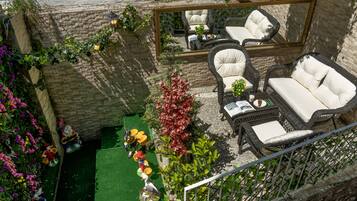 Una terraza en la azotea con mobiliario de mimbre, césped artificial verde y plantas decorativas.