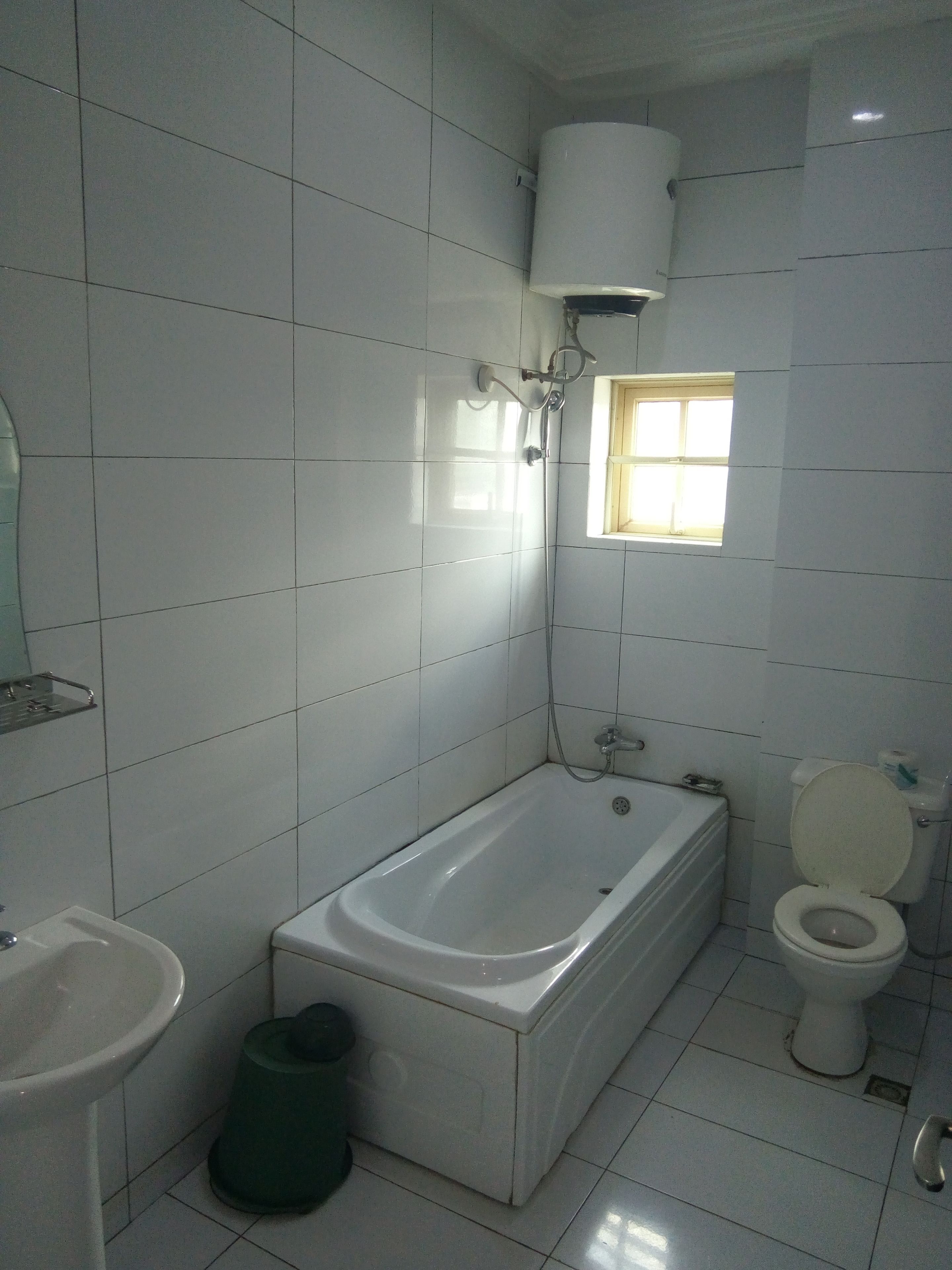 A bathroom with white tiles, a bathtub, a toilet, a sink, and a window.