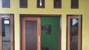 A building entrance with a wooden door, a green wall, and a tiled floor. - Kawah Ijen Guest House (Banyuwangi)