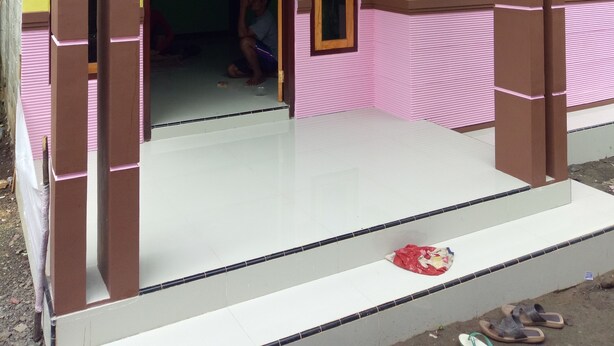 A building with a yellow and pink exterior, a white tiled entrance, and a brown structural framework. - Kawah Ijen Guest House (Banyuwangi)
