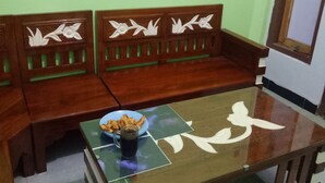 A wooden sofa with floral carvings, a glass coffee table with a magazine, and a bowl of snacks. - Kawah Ijen Guest House (Banyuwangi)