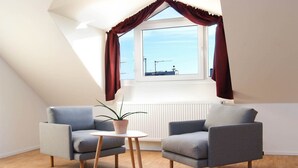 A modern, well-lit room with a sloped ceiling, two grey armchairs, a small round table, and a potted plant.
