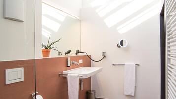 Ein modernes Badezimmer mit einem weißen Waschbecken, einem Spiegel, einem Handtuchhalter und einem Blumentopf.