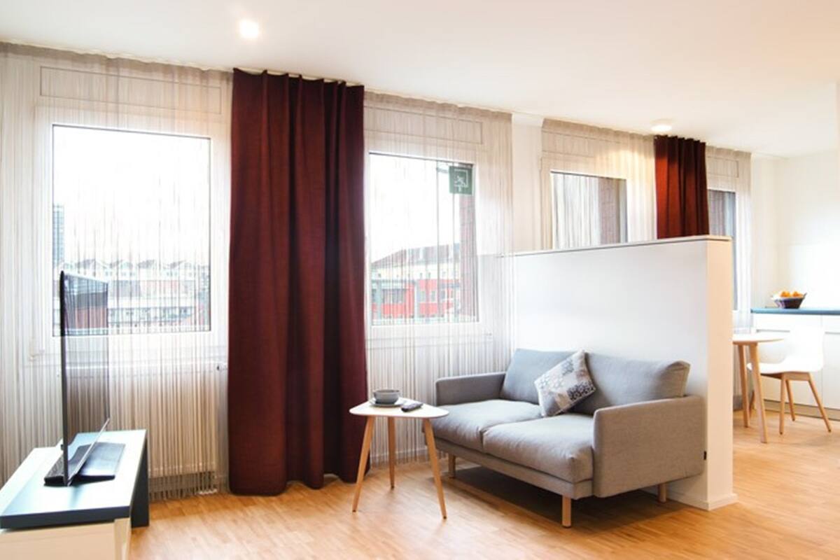 Une chambre d’hôtel moderne, dotée d’un canapé, d’une petite table et offrant une vue sur la ville grâce à de grandes fenêtres.