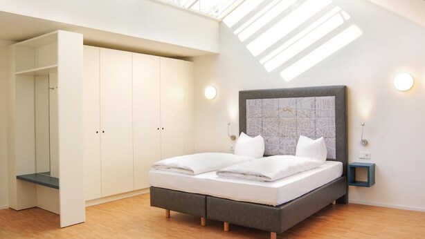 A bedroom with a skylight, a bed with white bedding, a grey headboard, and a map-themed wall.