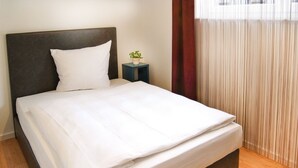 Una cama bien hecha con sábanas blancas en una habitación con piso de madera y cabecera oscura.