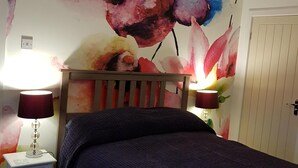 Una camera da letto con un letto, un comodino, una lampada e una parete con un dipinto floreale.