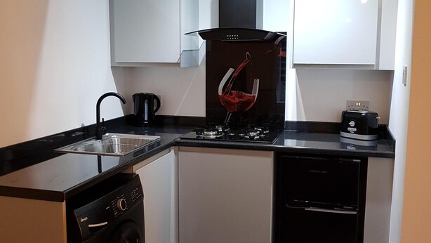Cucina compatta con lavatrice, macchina per il caffè e un bicchiere da vino sul bancone.