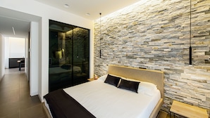 A modern bedroom with a stone wall, a large bed, and a glass door leading to a bathroom. - Acquarella Resort - Acquamarina Suite (TREVIGNANO ROMANO)