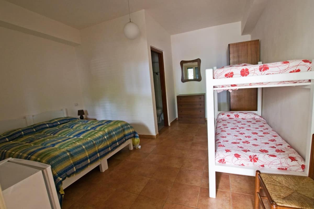 A dormitory room with two bunk beds, a small desk, and a mirror on the wall.