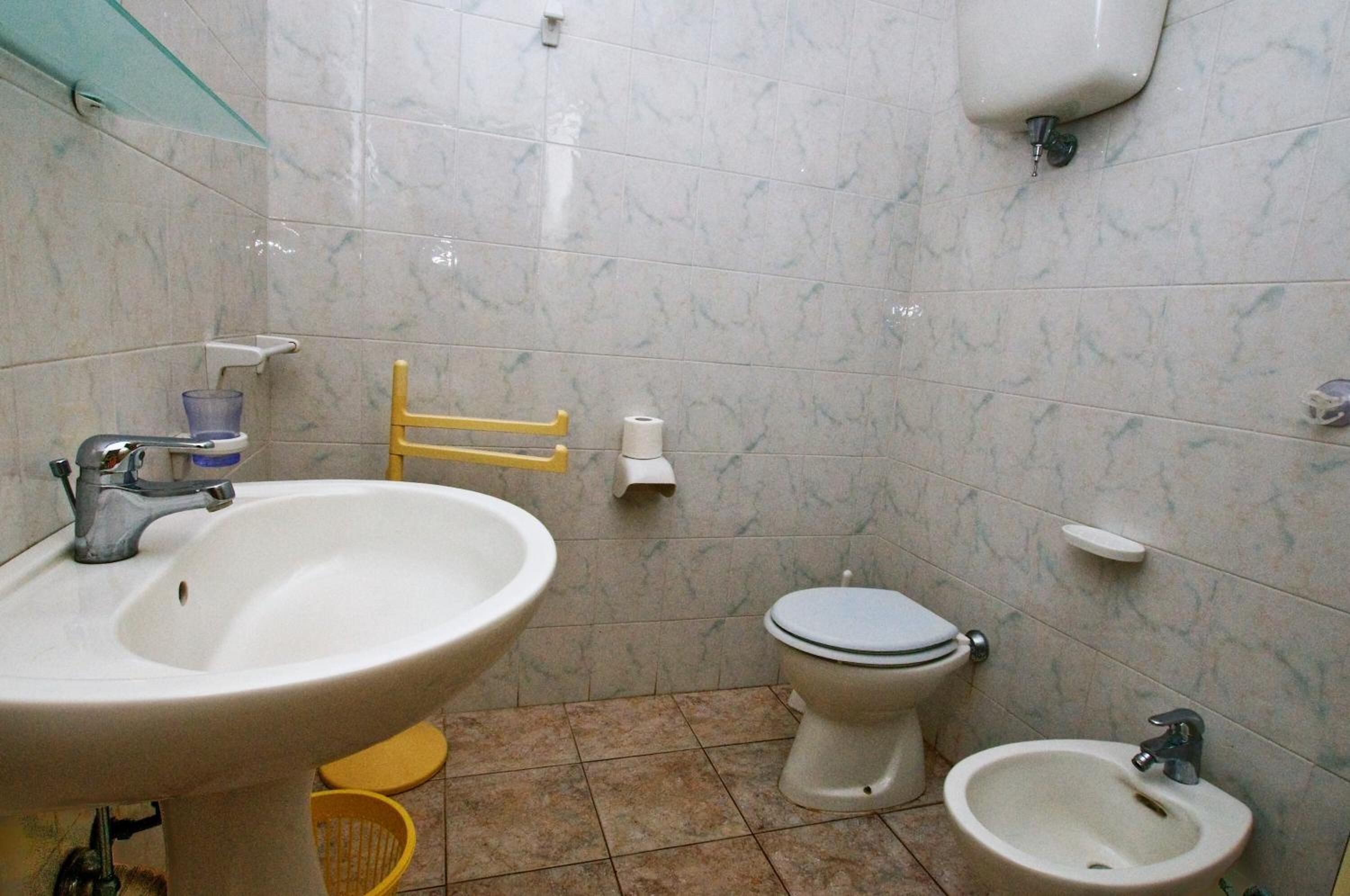 A bathroom with a sink, toilet, bidet, and a yellow chair.