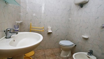 A bathroom with a sink, toilet, bidet, and a yellow chair.
