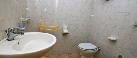 A bathroom with a sink, toilet, bidet, and a yellow chair.