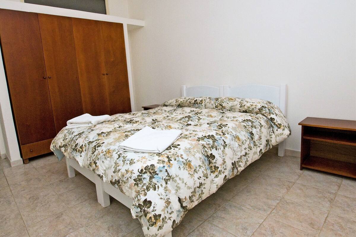 A bedroom with a bed, a wooden wardrobe, and a bedside table.