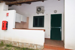 A building with a white exterior, a green door, a window with shutters, and a fire extinguisher mounted on the wall.