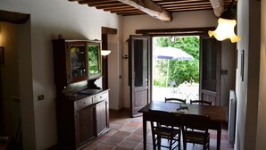A rustic kitchen with wooden beams, a dining table with chairs, and a view of greenery outside. - Agriturismo Marano (Gubbio)
