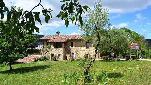 A stone house with a tiled roof, surrounded by a grassy lawn and trees. - Agriturismo Marano (Gubbio)