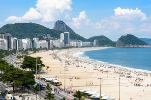 A beach with a cityscape in the background, including a prominent mountain and several high-rise buildings.