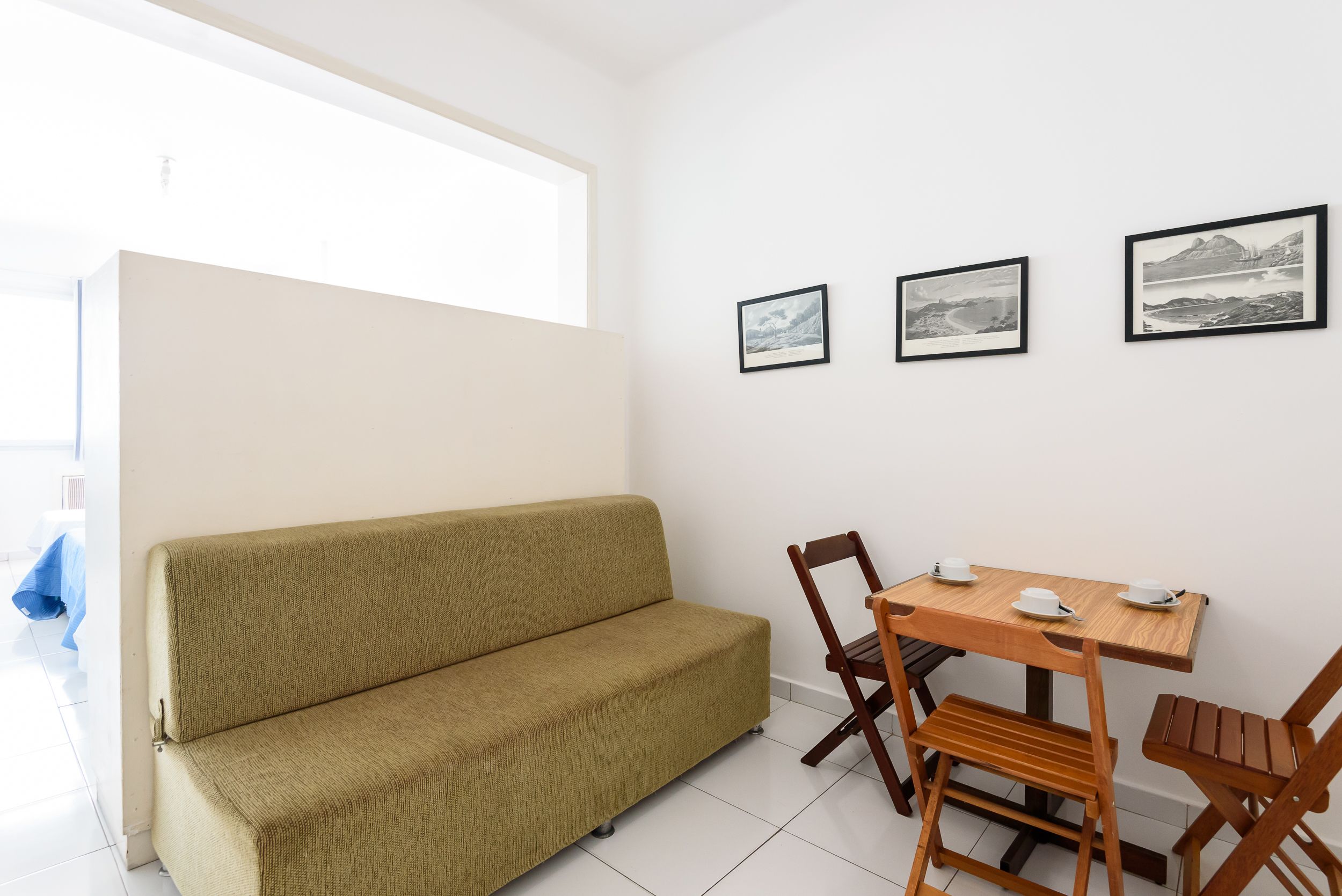 Een kamer met een beige bank, een houten eettafel met stoelen, en drie ingelijste foto's aan de muur.