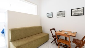 A room with a beige sofa, wooden dining table with chairs, and three framed pictures on the wall. - Omar do Rio - Apartamento A1202 (Rio de Janeiro)