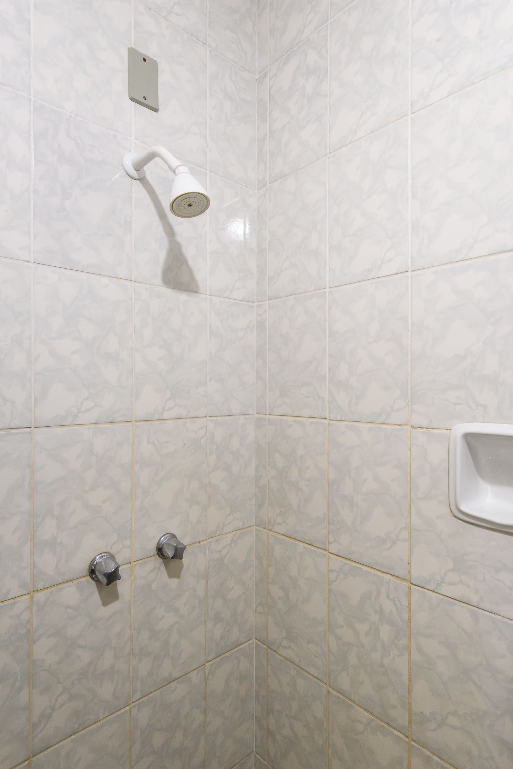A bathroom with white marble tiles, a showerhead, and a toilet.