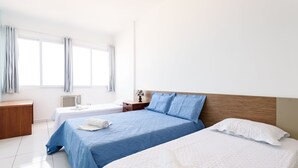 A hotel room with two beds, a wooden headboard, a bedside table, a nightstand, and a window with curtains. - Omar do Rio - Apartamento A1202 (Rio de Janeiro)