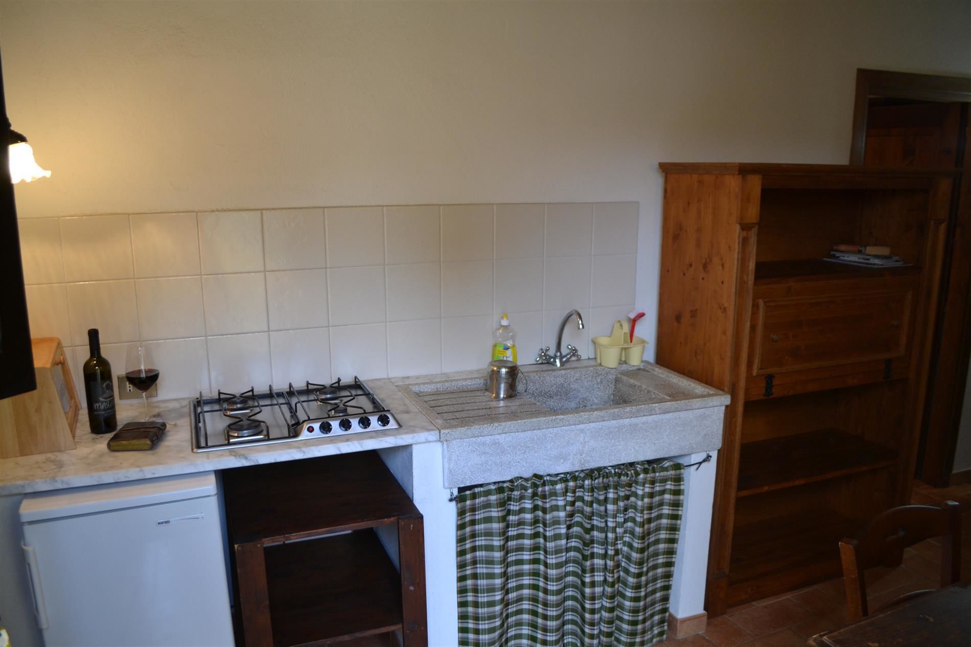 Een praktische keuken met een gasfornuis, een spoelbak en een kleine koelkast.