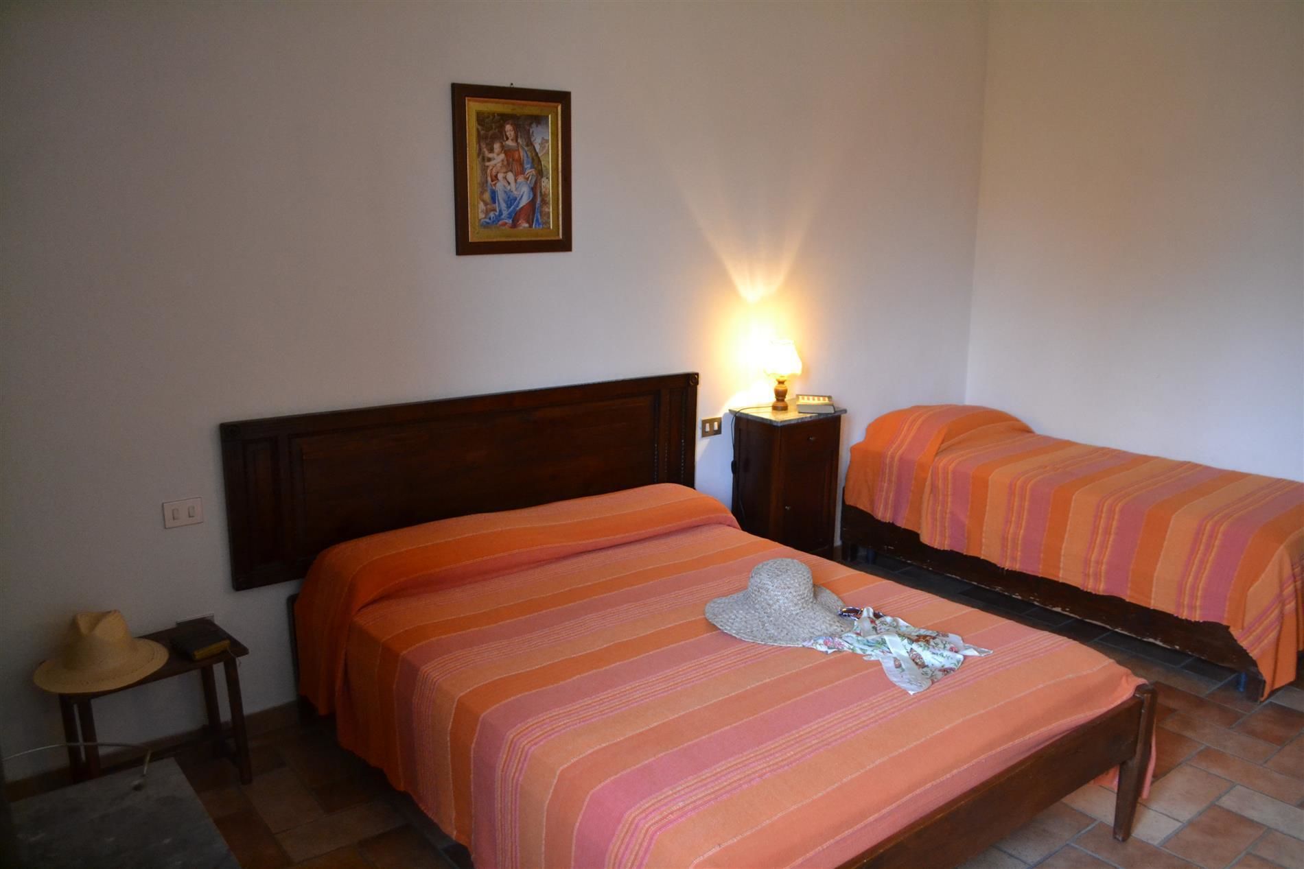 A room with two beds, each with an orange-striped bedspread. There is a wooden headboard on the left bed, a nightstand with a lamp, and a framed picture on the wall.