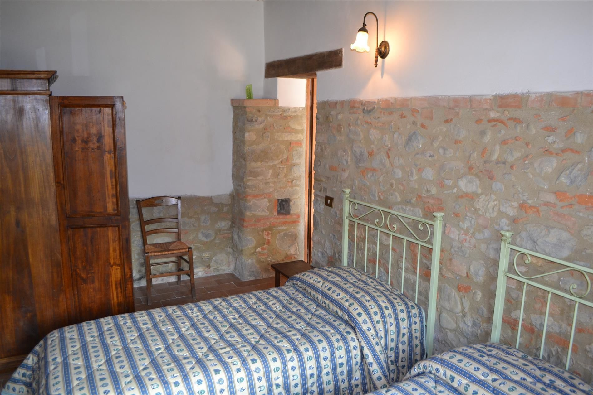 Camera da letto con parete in pietra, un armadio in legno, struttura del letto in metallo e coprip letto decorato.