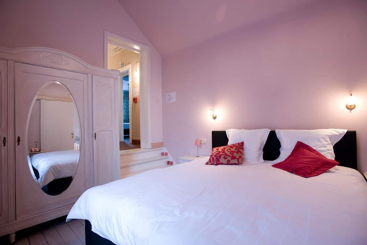 A bedroom with a large bed, a wardrobe with a mirror, and a staircase leading to an upper level.