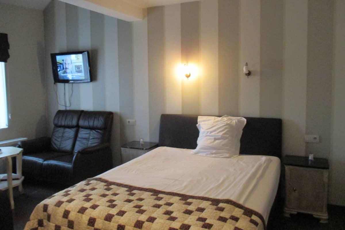 A hotel room with a bed, a chair, a television, and a nightstand.