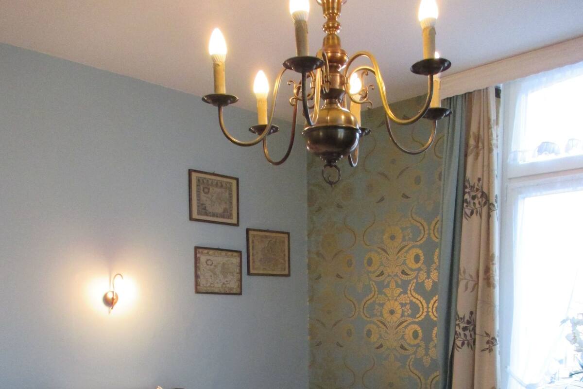 A bedroom with a bed, a nightstand, a wall-mounted light, and a window with curtains.