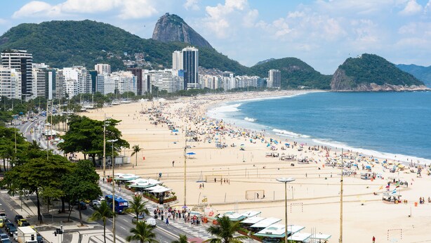 Une plage avec une vue sur la ville en arrière-plan, comprenant une montagne imposante et plusieurs immeubles de grande hauteur.