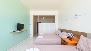 Une chambre d’hôtel avec deux lits, un téléviseur posé sur une étagère, un ventilateur de plafond et un placard avec des volets blancs.