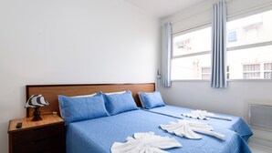 A hotel room with a large bed, a wooden nightstand, a lamp, and a window with curtains. - Apartamento A1206 - Omar do Rio (Rio de Janeiro)
