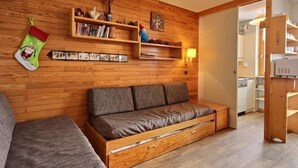 Una sala de estar acogedora con una pared de madera, un sofá gris y una estantería con diversos objetos.