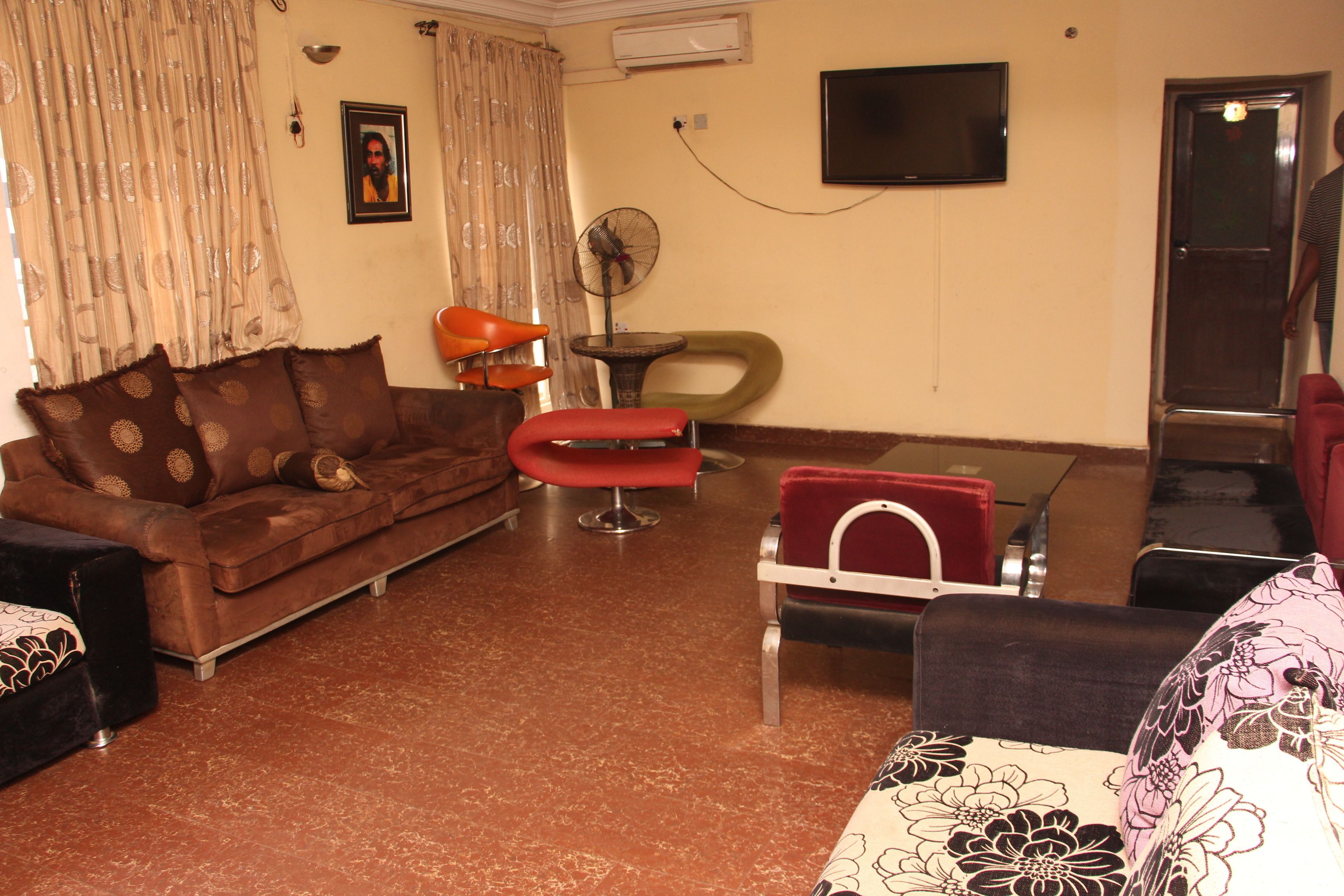 A living room with a brown sofa, a red chair, a small table, and a TV on the wall.