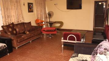 A living room with a brown sofa, a red chair, a small table, and a TV on the wall.